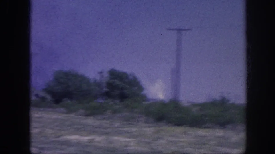 Side-window vehicle shot of roadside trees and a prominent utility pole, with bright haze or smoke glow at ground level, mid-1960s American highway, Southern United States.