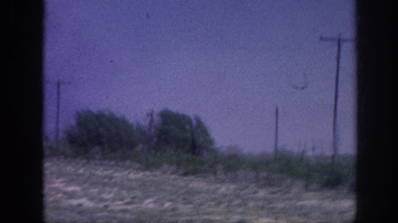 8mm home movie frame from what appears to be a rural area near Memphis, Tennessee, 1963 — a car window view of dry grassland, trees, and utility poles against a purple-shifted sky.