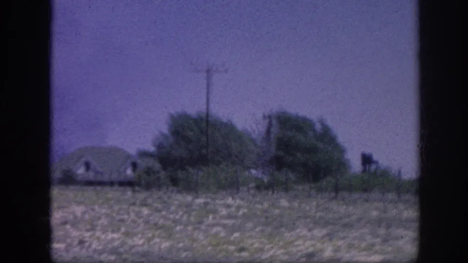 8mm home movie frame from what may be the Memphis area, 1963 — a low building or structure appears among trees and dry fields through a moving car window.