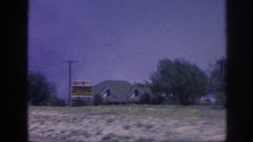 8mm home movie frame from what may be a rural highway near Memphis, 1963 — a roadside commercial sign and low structure visible through a moving car window.