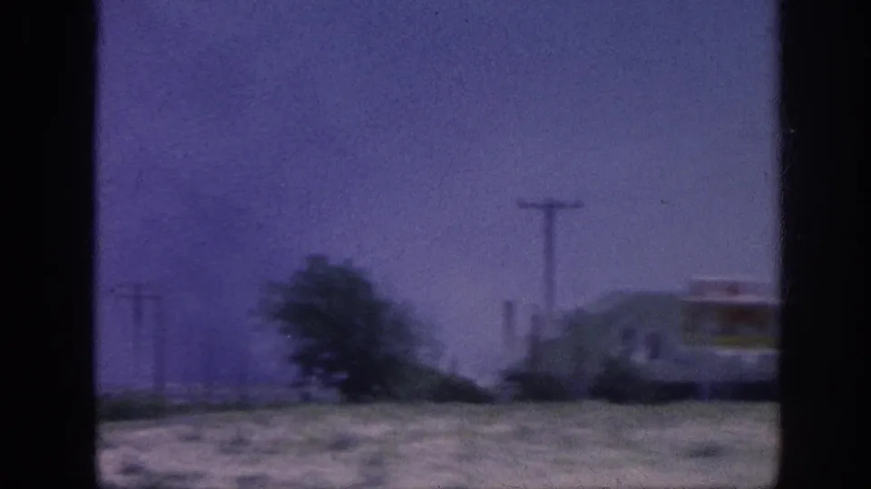 8mm home movie frame from what may be a rural highway near Memphis, 1963 — trees and a partially visible roadside sign appear at the right as the vehicle moves past.