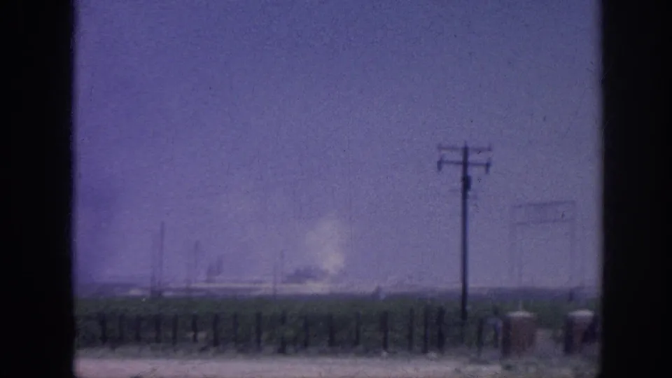 8mm home movie c.1963, open rural landscape through window: telephone poles, field with low vegetation, distant smoke plume, strong purple dye shift.