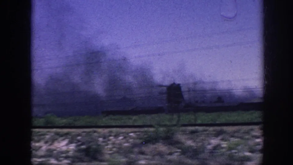 8mm home movie, c.1963 Memphis, Tennessee — dark smoke columns rise over flat scrubland with silhouetted utility poles, shot through a moving vehicle window.
