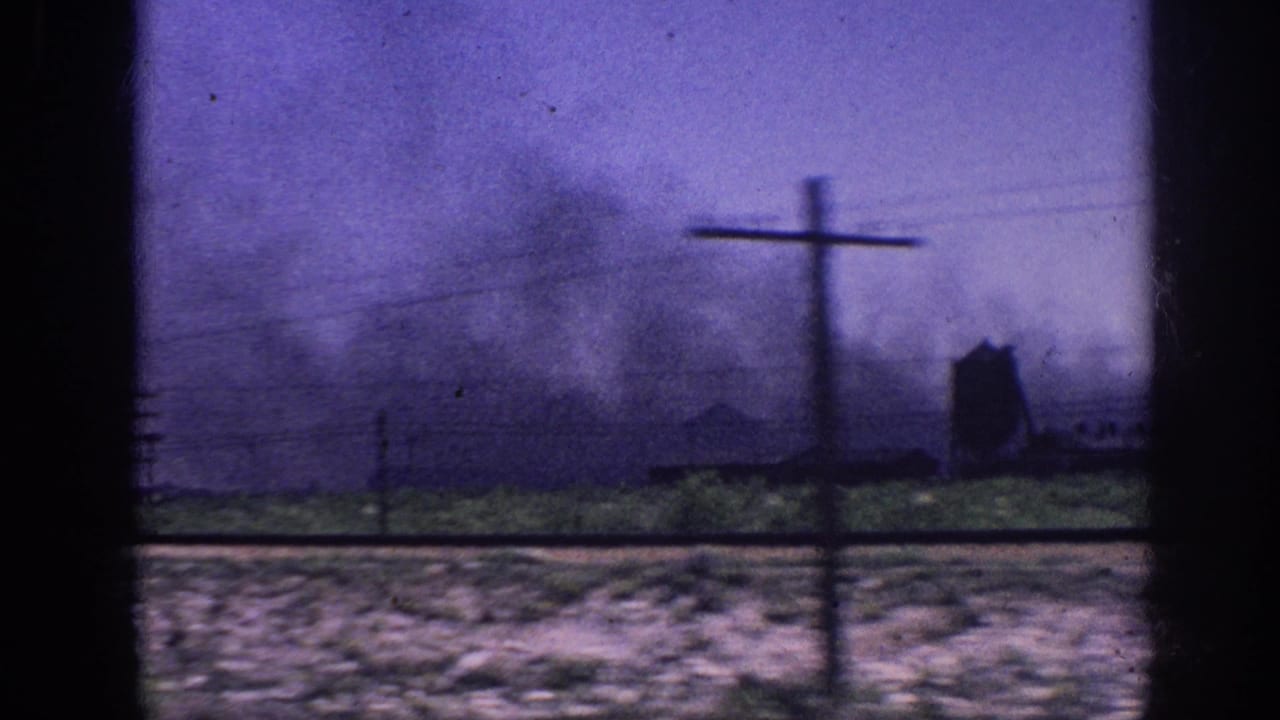 Smoke rising; prominent utility pole with crossbar right of frame; faint dark structure silhouetted in background; purple-cast 8mm sky.