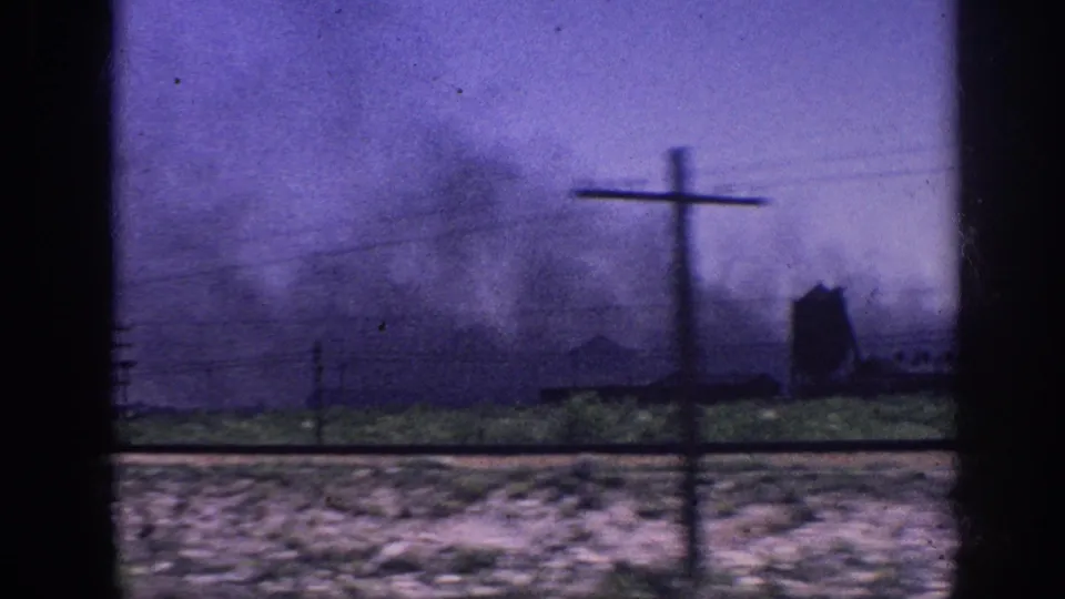 8mm home movie, c.1963 Memphis — smoke column beside a silhouetted utility pole with crossbar and a faint background structure against a purple-cast sky, from a moving vehicle.