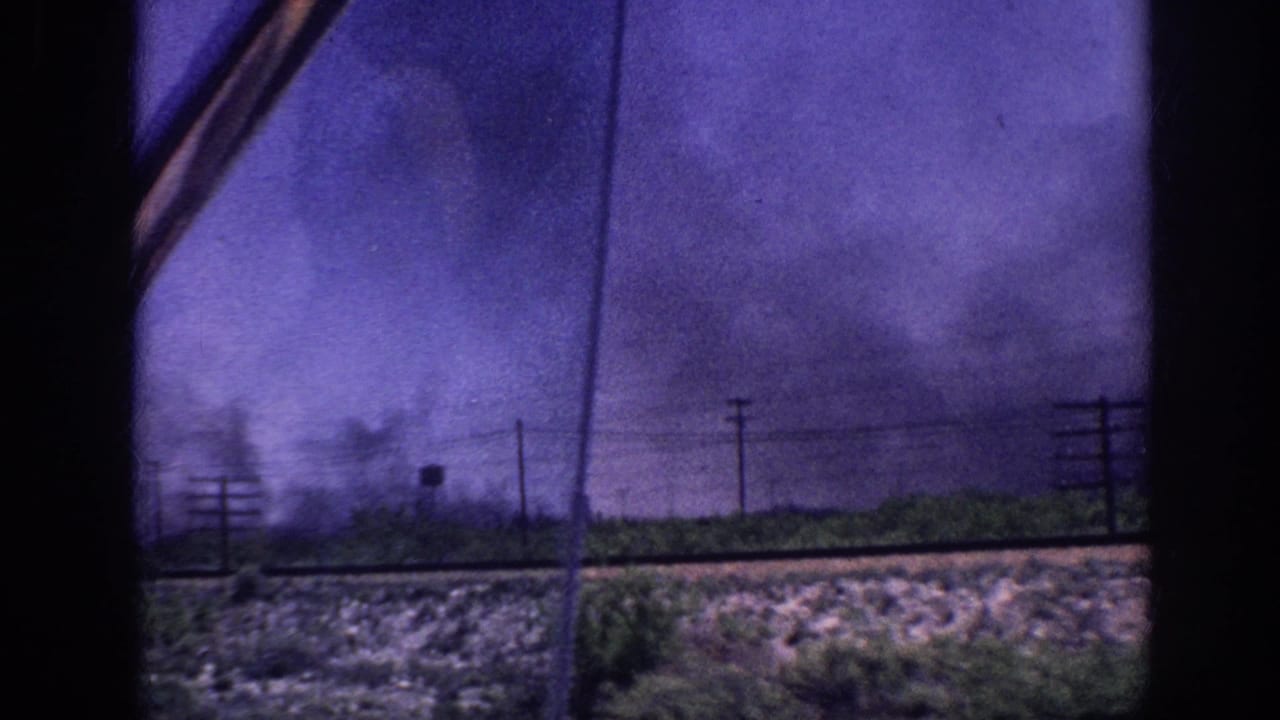 Purple storm sky with advancing dark clouds over flat terrain and utility poles, shot through a vehicle window.