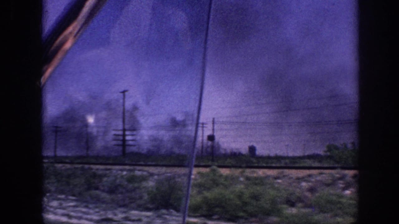 1963 Memphis, Tennessee area: view through a moving vehicle window of a roadside with utility poles and large dark smoke plumes under a color-shifted purple sky.