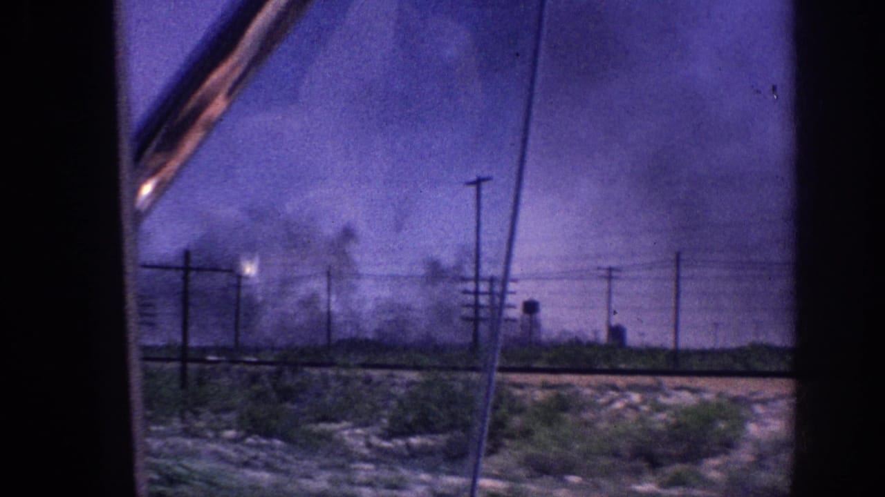 1963 Memphis, Tennessee area: vehicle window shot of roadside utility poles with multiple smoke plumes and a bright flare-like light source under a color-shifted purple sky.