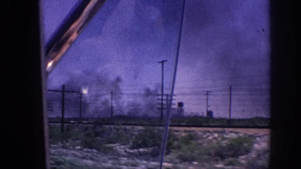 1963 Memphis, Tennessee area: vehicle window shot of roadside utility poles with multiple smoke plumes and a bright flare-like light source under a color-shifted purple sky.