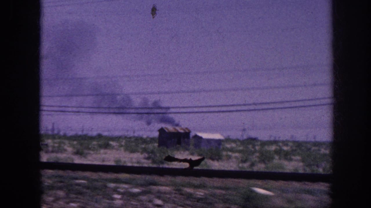 Through a moving vehicle's window, a small wooden outbuilding sends dark smoke skyward across flat rural terrain; 8mm footage metadata places this in the Memphis, Tennessee area, 1963.