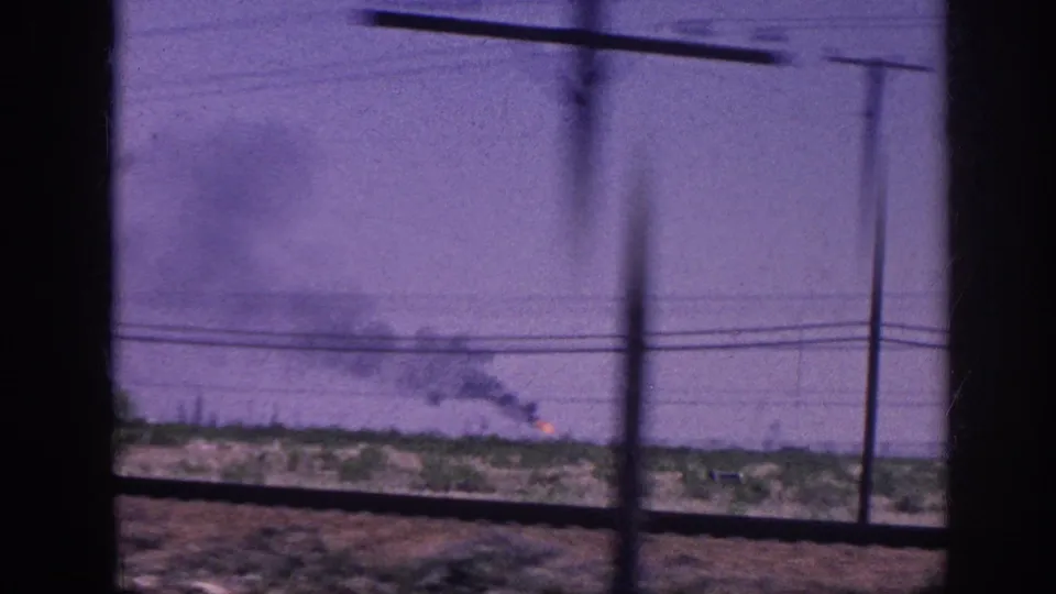 View through a moving vehicle window of rural terrain with multiple rising smoke plumes and orange fire glow at the horizon; 8mm footage with purple dye shift and motion blur, circa 1963.