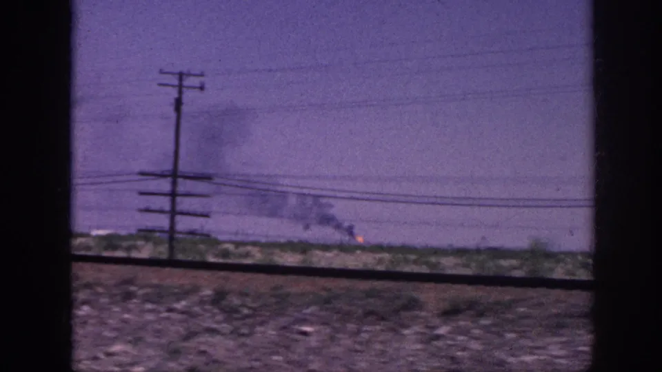 From a moving vehicle, continued smoke rises over flat rural terrain with utility poles and power lines crossing the purple-shifted 8mm frame; metadata places this near Memphis, Tennessee, 1963.