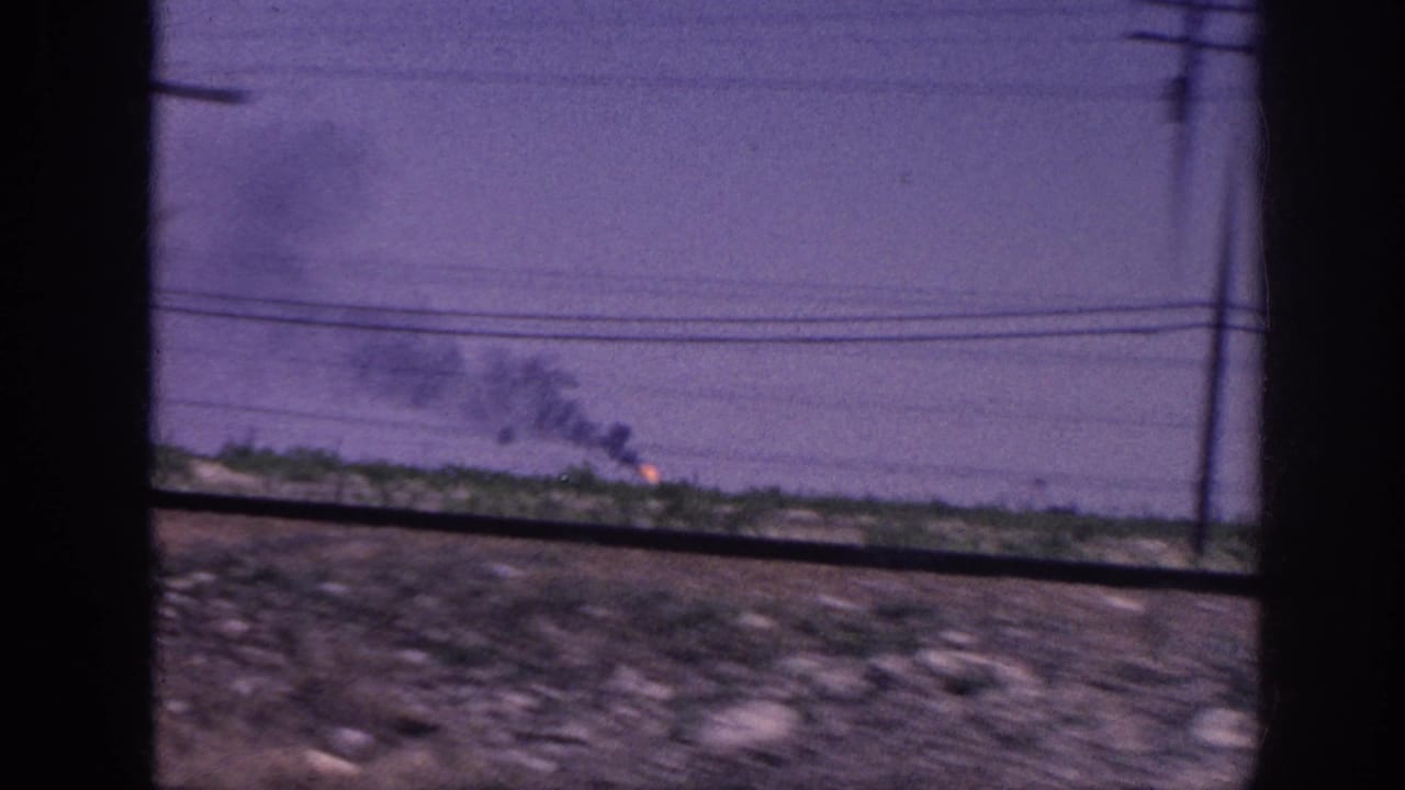 8mm car-window view of flat rural terrain with a telephone pole at the right edge and fire burning on the far horizon, likely rural Tennessee circa 1963.