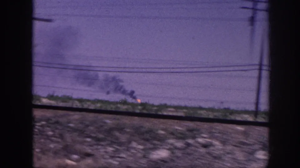8mm car-window view of flat rural terrain with a telephone pole at the right edge and fire burning on the far horizon, likely rural Tennessee circa 1963.