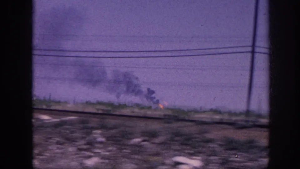 8mm car-window shot of rural landscape showing multiple fires burning on the far horizon with drifting smoke and a telephone pole at the right edge, likely Tennessee circa 1963.