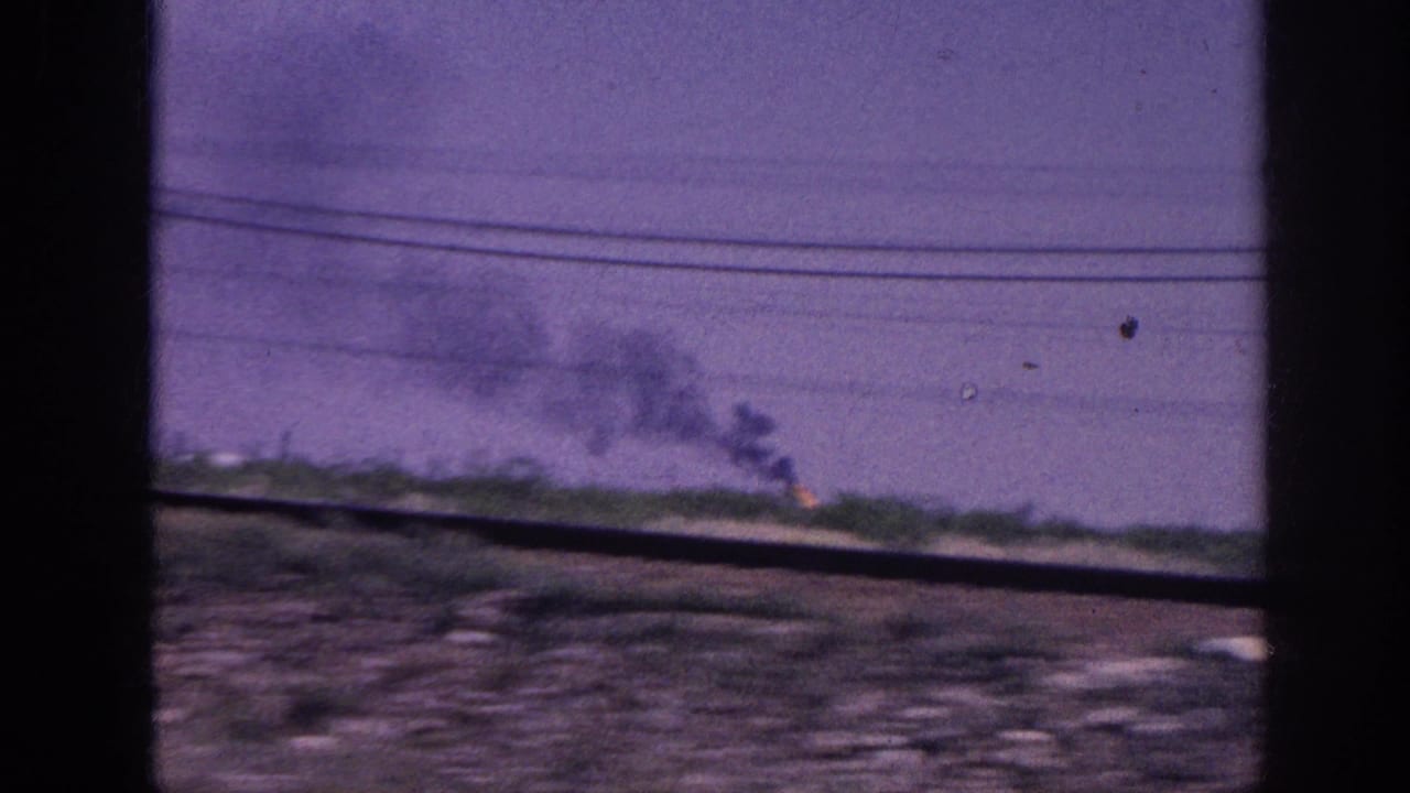 1963 8mm home movie: distant fire with dark smoke columns rising into a purple-cast sky, shot from a moving vehicle near Memphis, Tennessee.