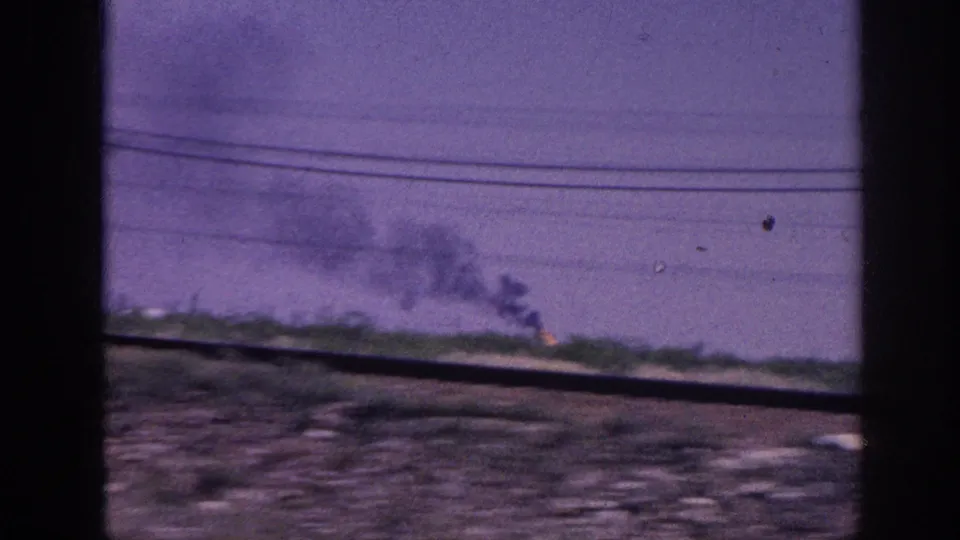 1963 8mm home movie: distant fire with dark smoke columns rising into a purple-cast sky, shot from a moving vehicle near Memphis, Tennessee.