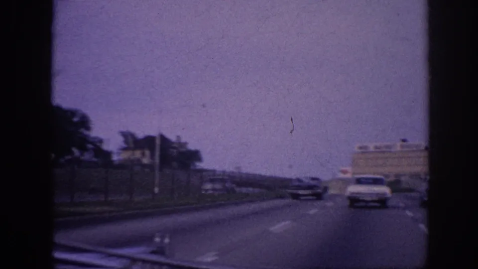 Memphis freeway, 1963 — open multi-lane road with a light-colored sedan ahead; industrial buildings and distant signage visible on the horizon.