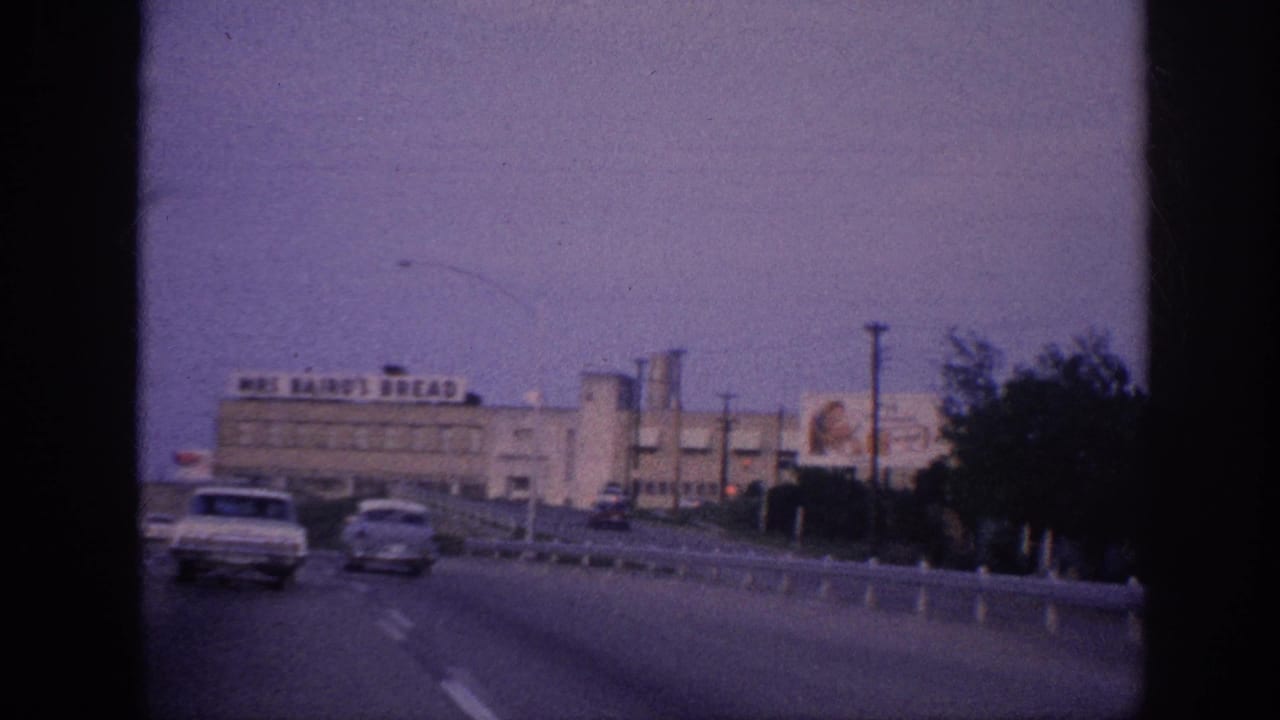 Moving highway view with cars and a large Mrs Baird's Bread building beside the road.