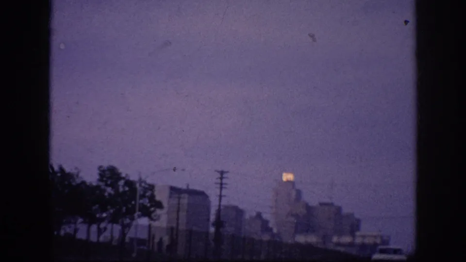A final Memphis dusk view shows the distant skyline beyond roadside trees and utility poles, with a car entering the lower-right edge of the soft, purple-shifted 8mm frame.