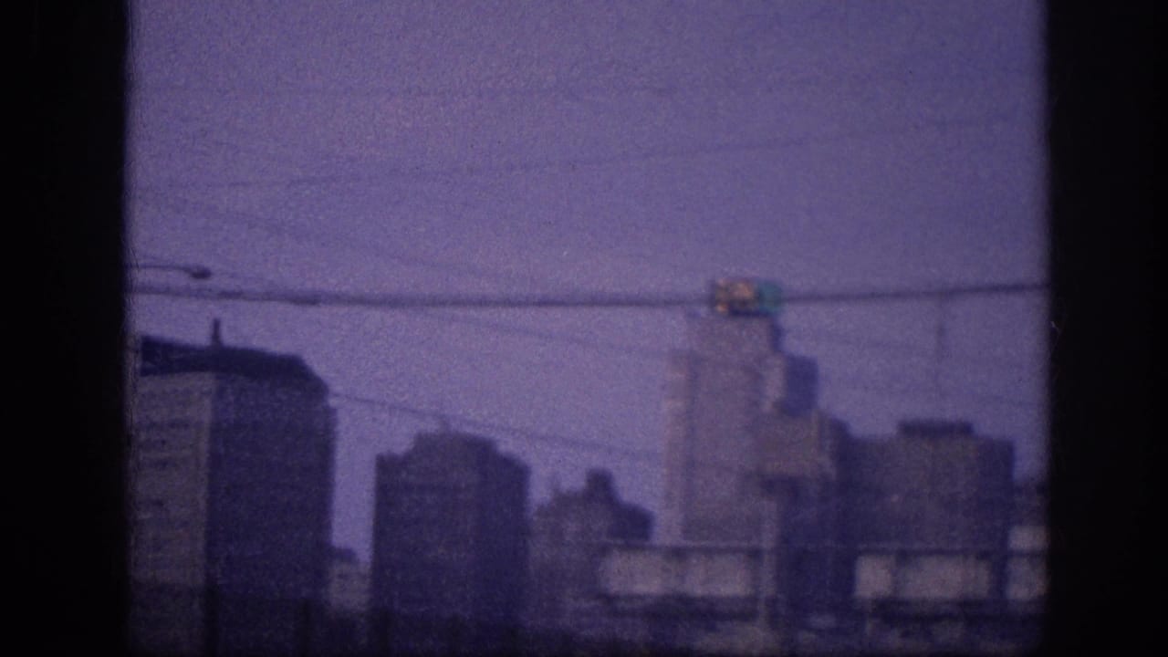 Purple-tinted 8mm frame showing a mid-century downtown skyline with overhead power lines and a traffic signal in the upper portion.