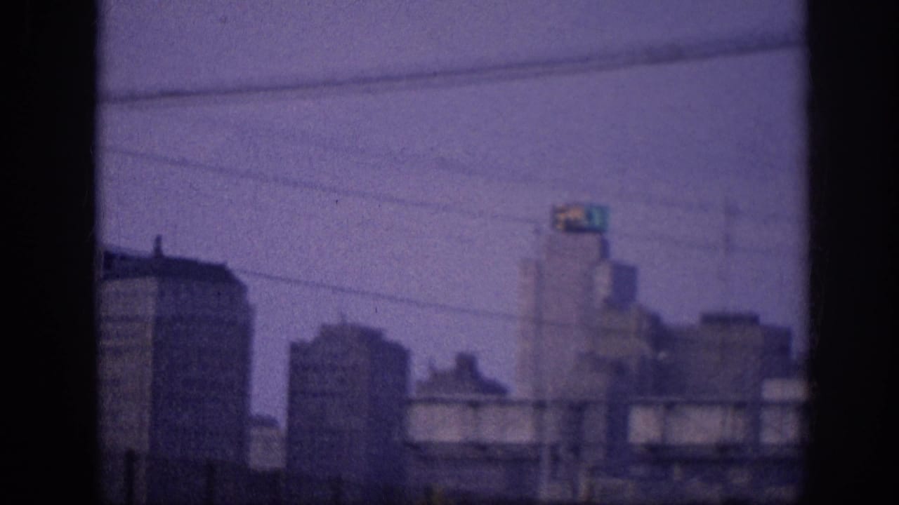 Purple-tinted 8mm frame showing the same city skyline from a moving vehicle, with utility lines crossing the upper frame.