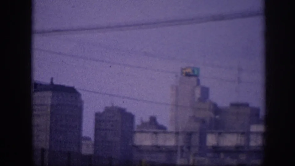 Slightly shifted 8mm view of a mid-century downtown skyline from a moving vehicle, showing multi-story commercial buildings and utility lines, Memphis c. 1963.