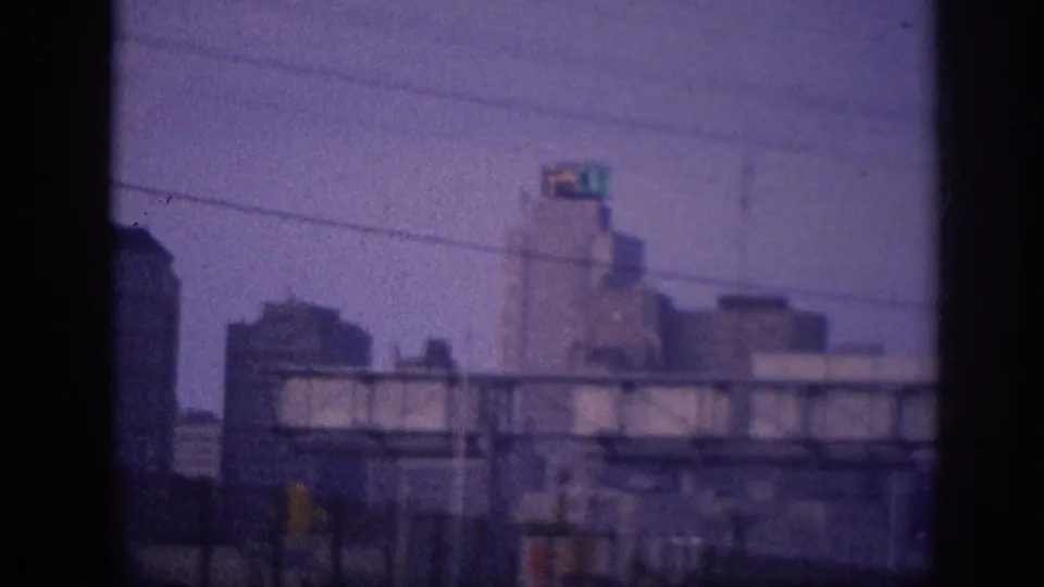 Downtown skyline receding as a steel highway sign gantry enters frame from a moving vehicle, Memphis c. 1963, 8mm home movie.