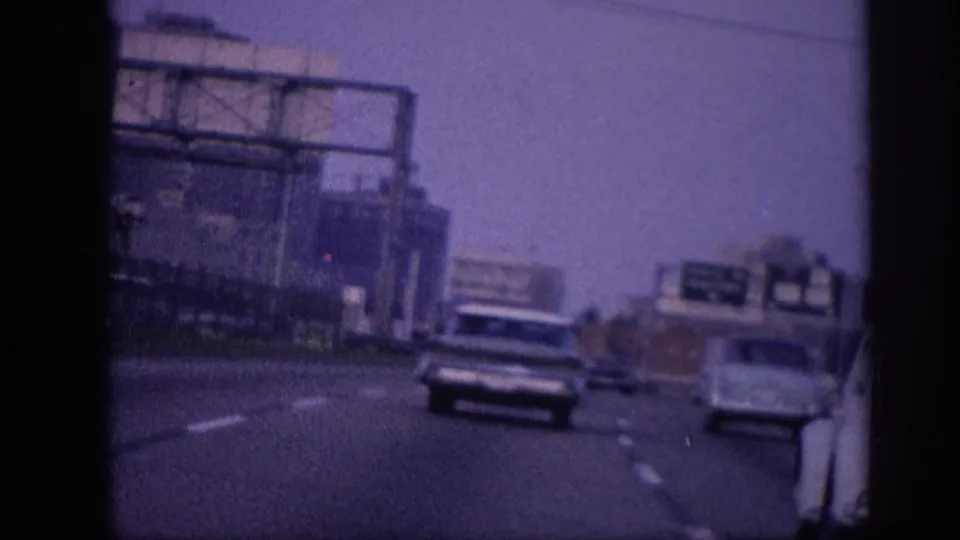 Multi-lane highway with 1960s American automobiles and a large overhead sign gantry; mid-century city buildings visible in the background, Memphis c. 1963.