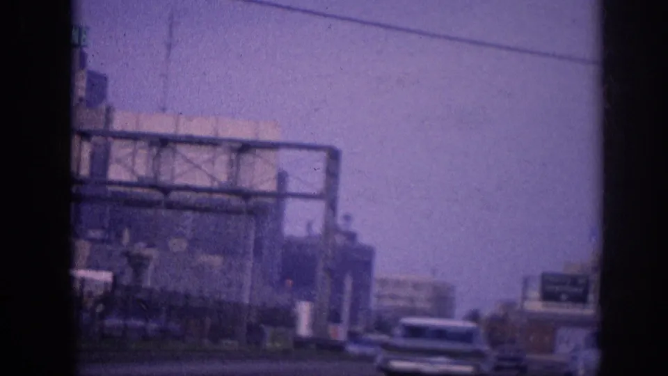 8mm shot from inside a moving vehicle showing multiple early-1960s American sedans in highway traffic, a large metal sign gantry overhead, and urban commercial buildings, Memphis, Tennessee, circa 1963.
