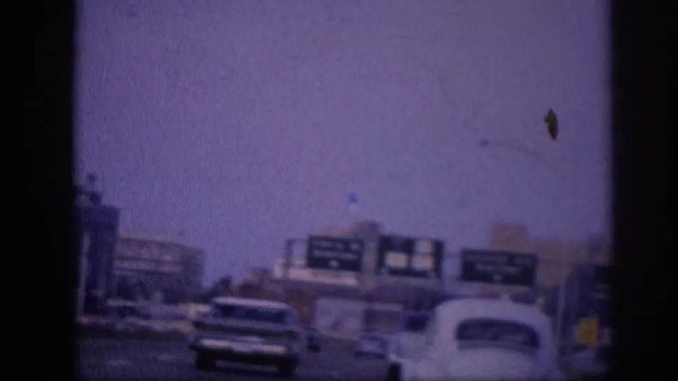 8mm driving footage showing a prominent white early-1960s American sedan in the foreground, green overhead highway directional signs, and urban buildings in the background, Memphis circa 1963.