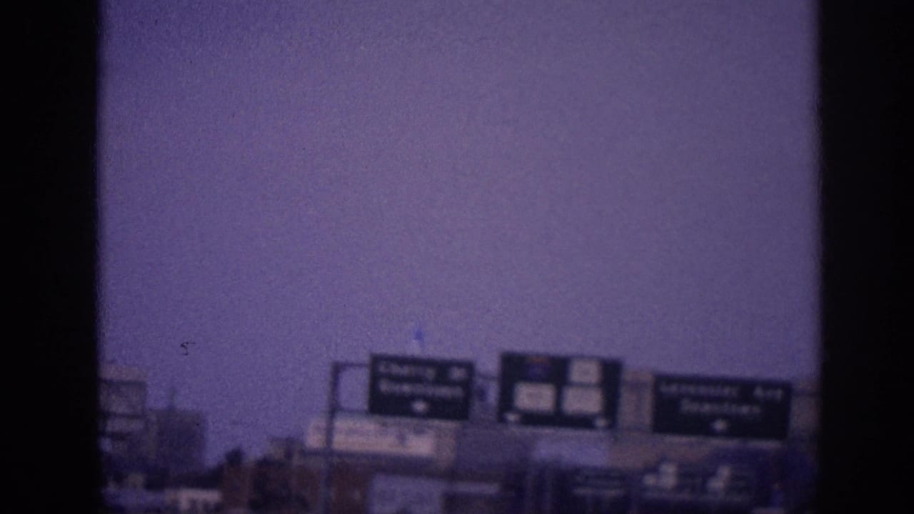 Soft overhead road signs against a purple-tinted sky with dark film-frame borders.