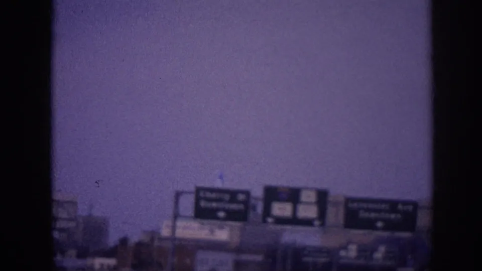 1963 Memphis 8mm frame showing overhead highway signs for Cherry Street and Lancaster Avenue Downtown under a purple-tinted sky.