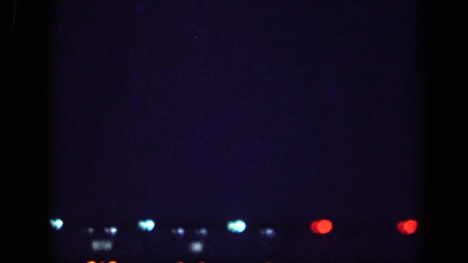 8mm home-movie frame from 1963, likely Memphis, Tennessee: a horizontal row of out-of-focus blue, white, and red lights across a deep blue night sky.