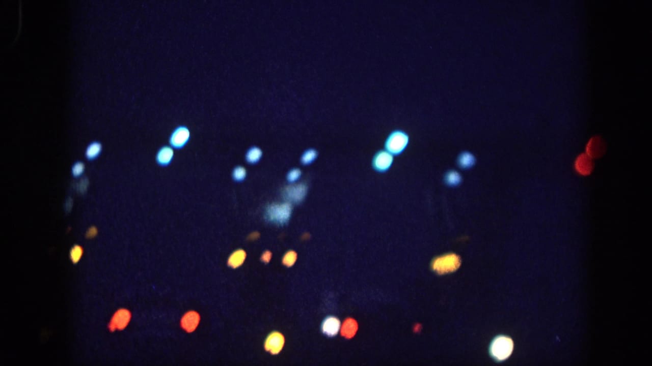 8mm home movie frame circa 1963 showing bokeh light orbs from vehicle headlights, taillights, and street lights against a night sky, attributed to Memphis, Tennessee.