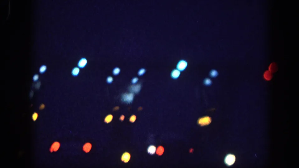 8mm home movie frame circa 1963 showing bokeh light orbs from vehicle headlights, taillights, and street lights against a night sky, attributed to Memphis, Tennessee.