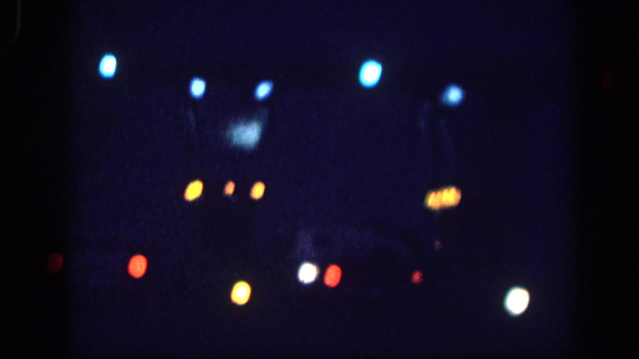 Out-of-focus city night with blue, amber, and red bokeh orbs and faint upper-frame silhouette detail on a deep blue field.