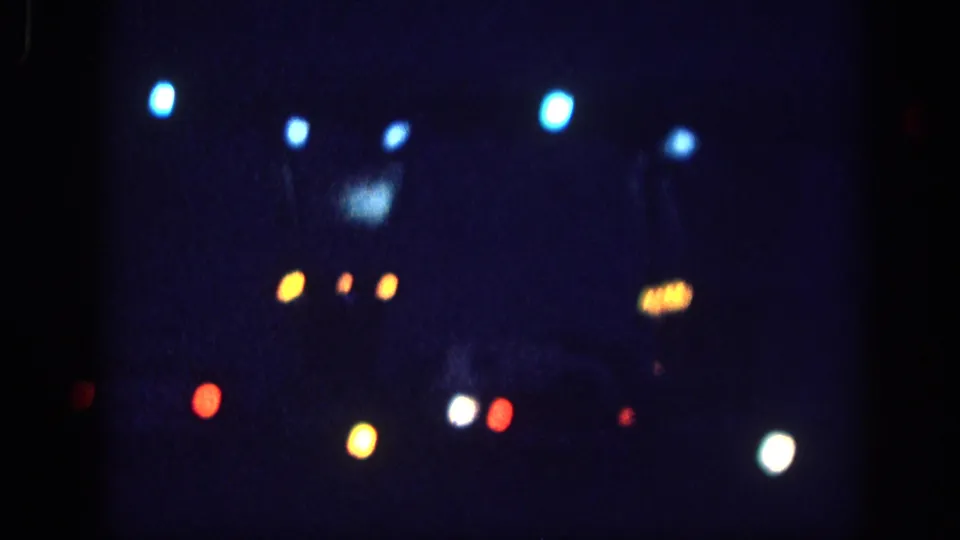 8mm home movie frame circa 1963 showing mixed vehicle and street-light bokeh with a faint dark silhouette visible at upper frame, attributed to Memphis night.