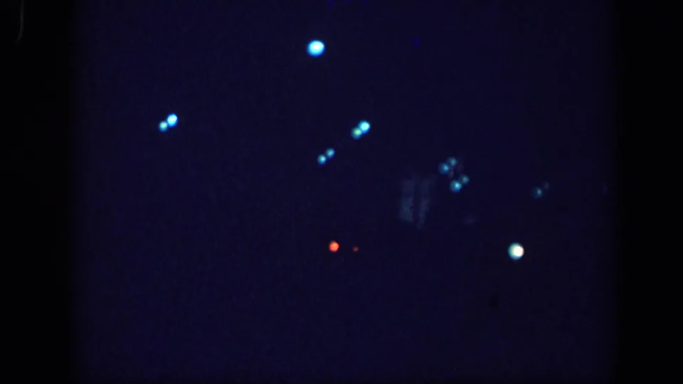 8mm home movie frame circa 1963 with sparser bokeh light distribution, suggesting camera movement or a shift in the night driving scene.