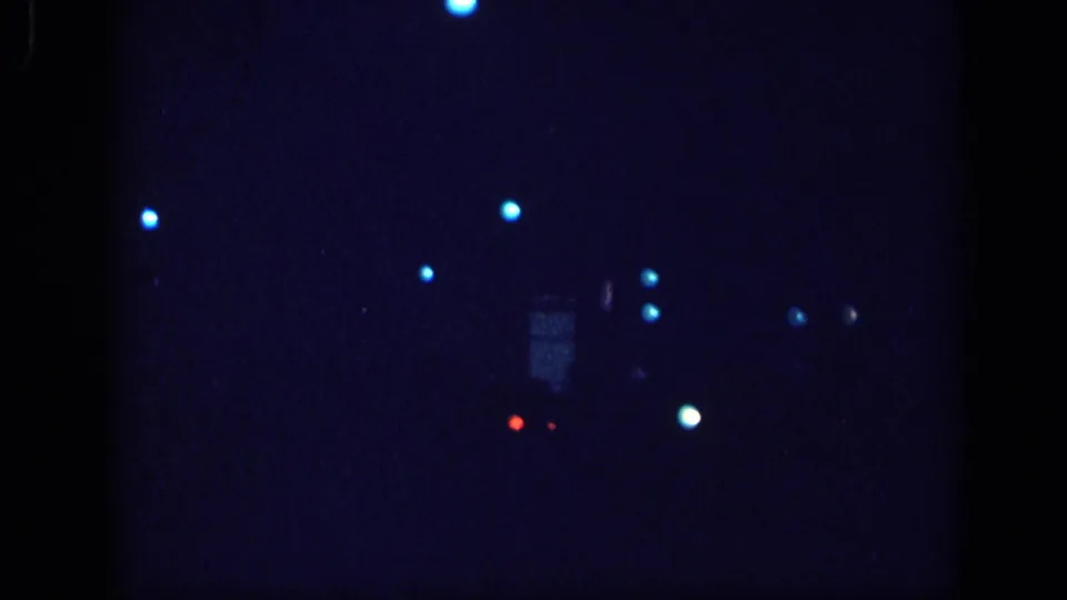 8mm home movie frame circa 1963 showing a near-dark field with sparse bokeh light points, possibly the tail end of a night driving sequence.
