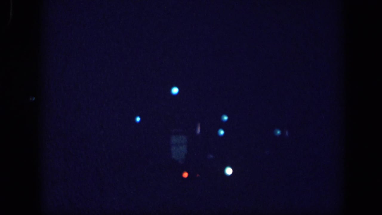 Near-black 8mm film frame with scattered cyan and white bokeh light points against a deep blue field.