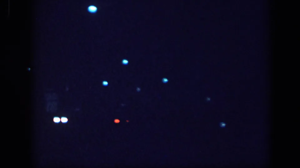 8mm night-drive frame from a 1963 Memphis home movie; paired white headlights at lower left and red-orange taillights suggest passing traffic on a dark street.
