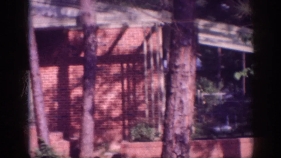 Brick mid-century residence or low-profile building with a covered overhang, shaded by mature trees, circa 1963 Memphis; pronounced magenta film aging visible.