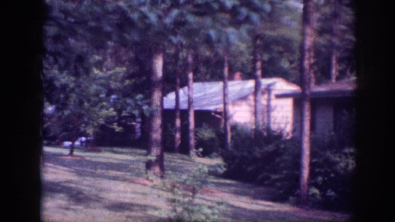 Low single-story camp or retreat building among tall pines, possibly Memphis Tennessee area circa 1963, on aged 8mm film with characteristic lavender color shift.