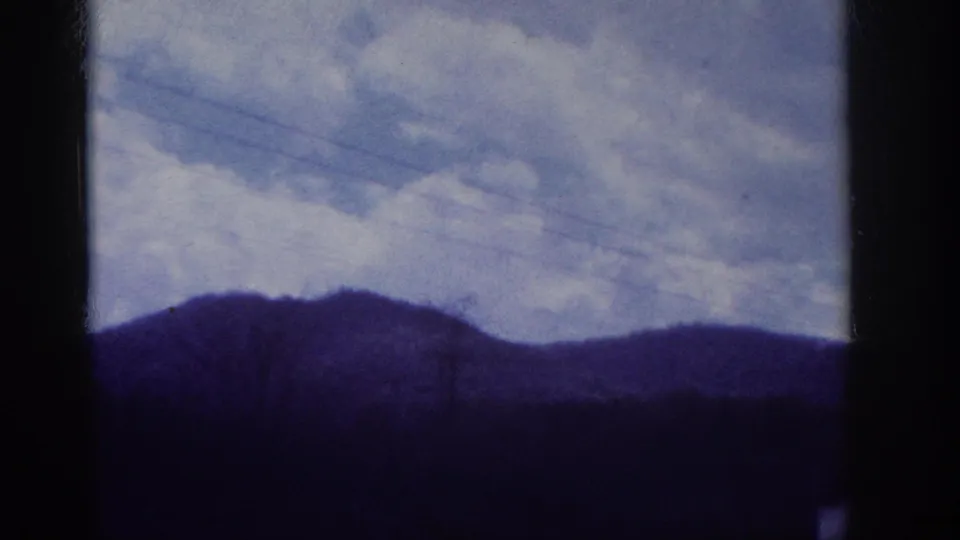 Low hills with diagonal utility power lines and overcast sky, shot through a car window on 8mm home movie film; consistent with a southeastern US road journey c. 1963.