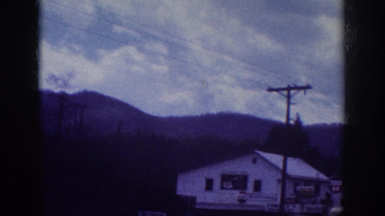 8mm home movie frame showing a white roadside commercial building with period signage and a utility pole against wooded hills, attributed to Memphis, Tennessee area, circa 1963.