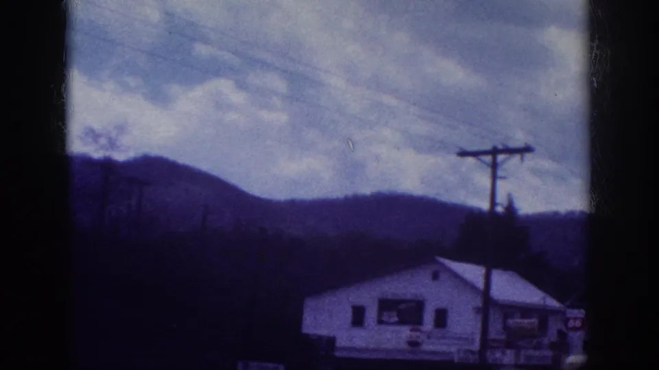 8mm home movie frame showing a white roadside commercial building with period signage and a utility pole against wooded hills, attributed to Memphis, Tennessee area, circa 1963.