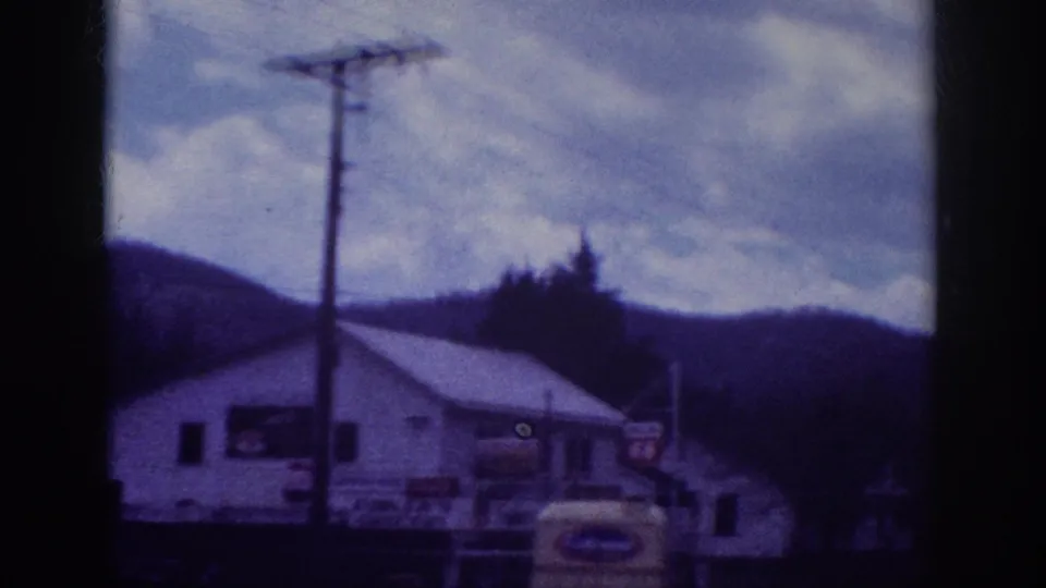 8mm pan frame showing commercial signage on a white building, a utility pole, and a partial yellow vehicle against wooded hills, attributed to Memphis, Tennessee, circa 1963.