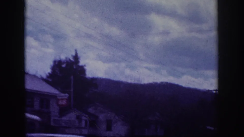 Mid-pan 8mm frame showing a smaller pitched-roof building, utility pole, bare trees, and rolling hills under overcast sky, attributed to Memphis, Tennessee area, circa 1963.