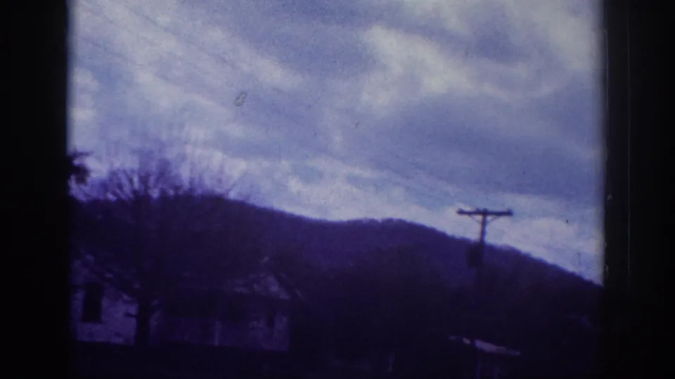 End-of-pan 8mm frame dominated by layered overcast clouds above rolling wooded hills and a lone utility pole, attributed to Memphis, Tennessee area, circa 1963.